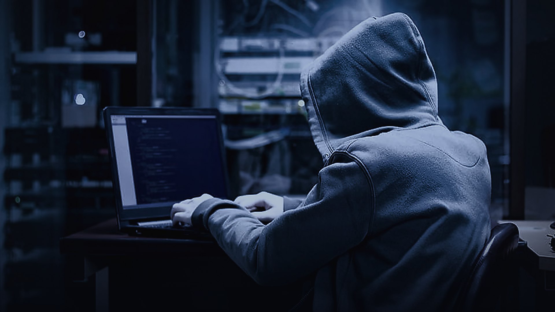 Sunucu odasında açık gri kapüşonlu bir kişi dizüstü bilgisayarda çalışıyor — white hacker temalı temsili görsel
